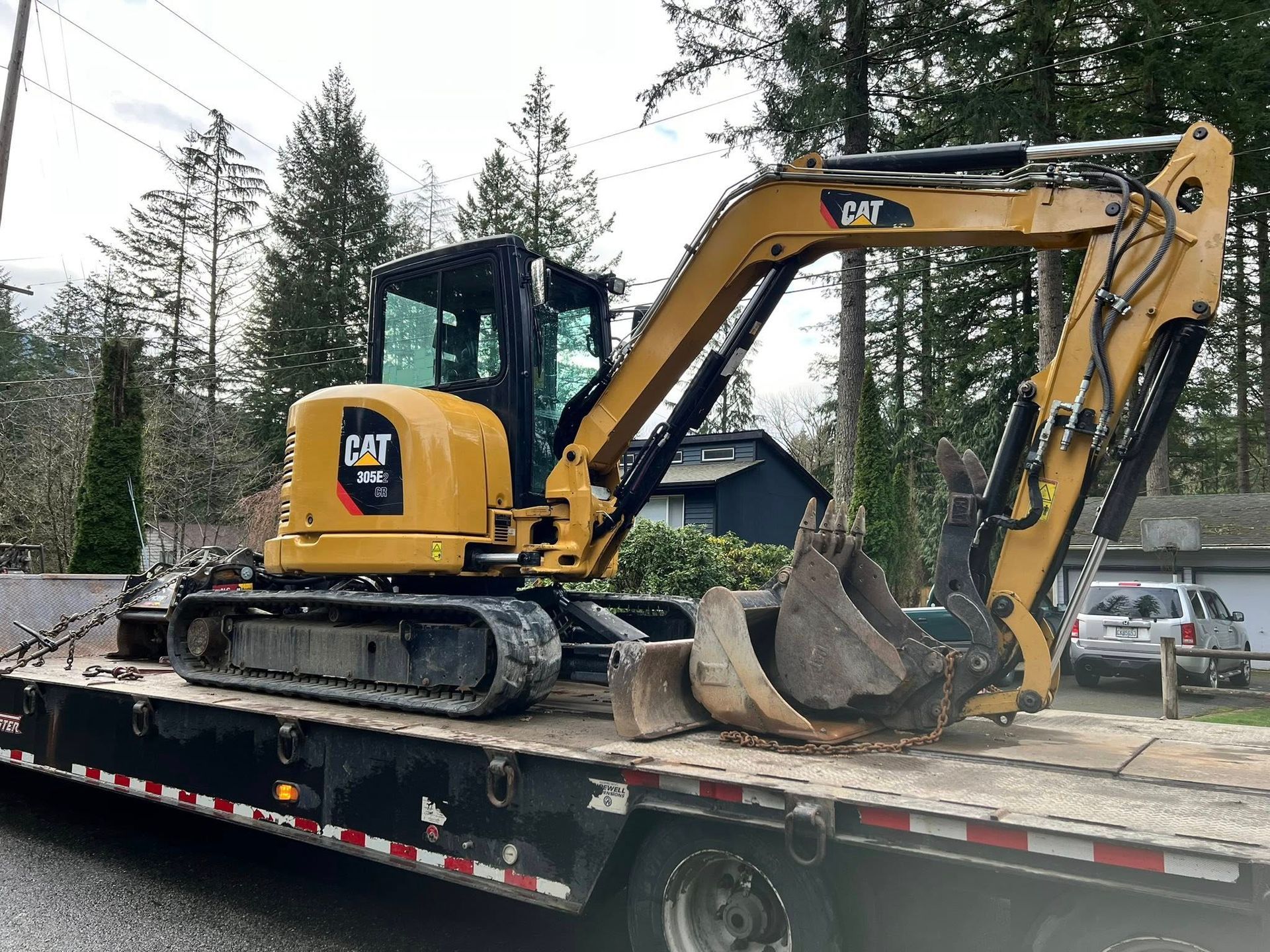 A yellow Caterpillar 308 excavator secured on a flatbed trailer outdoors, with a bucket resting on the deck.