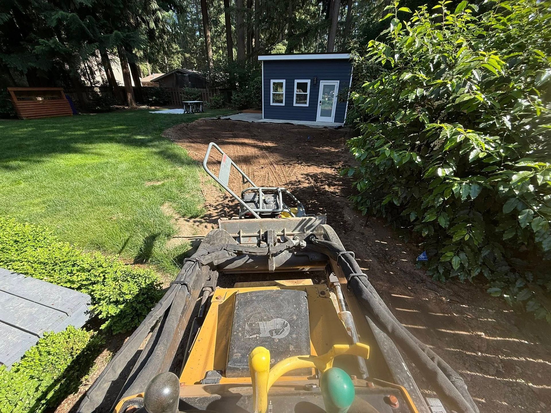 A view from a yellow riding lawn mower looking toward a small blue shed in a grassy backyard.