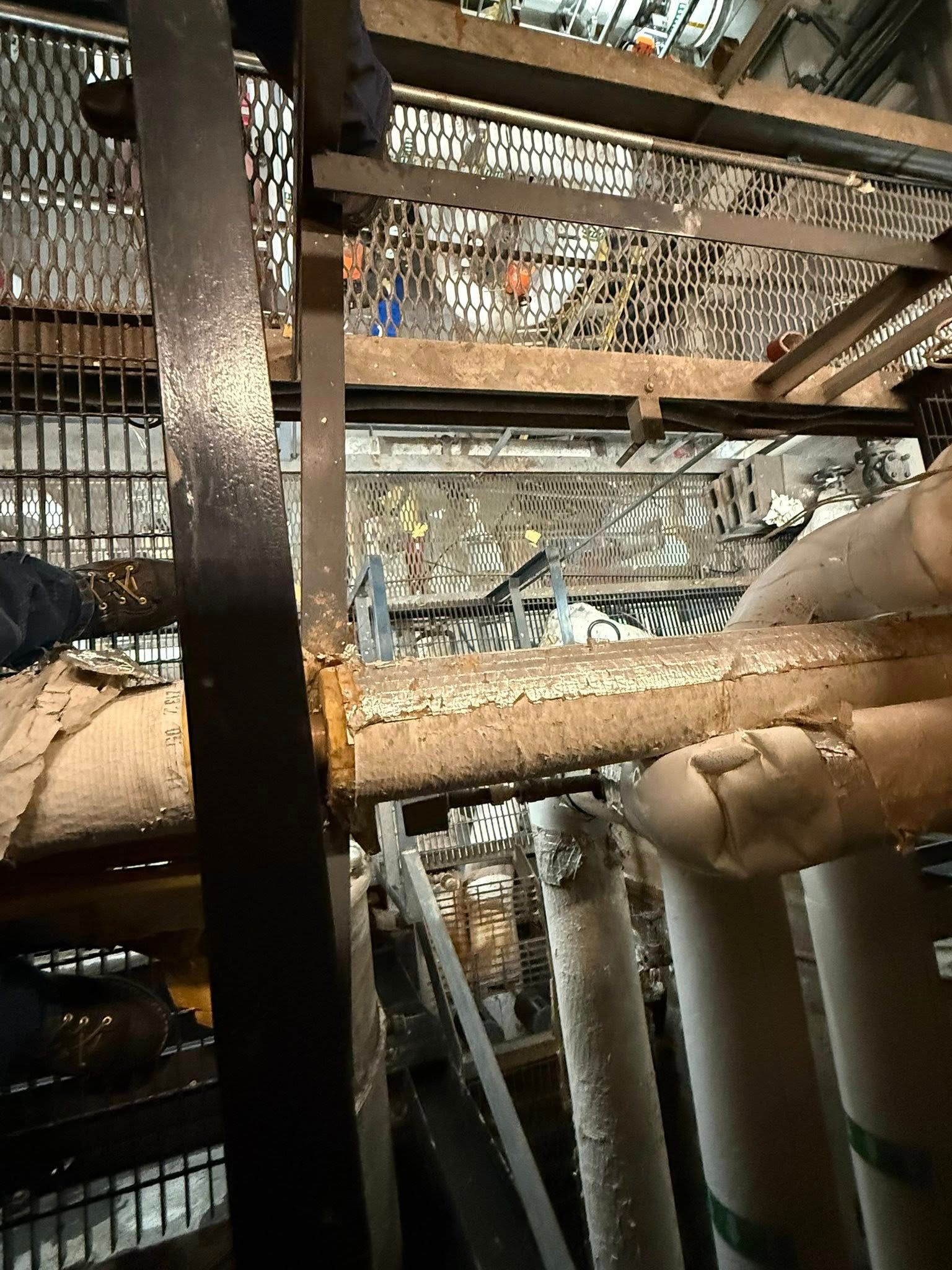 A close-up view of industrial piping with textured, worn insulation running horizontally through a metal framework.