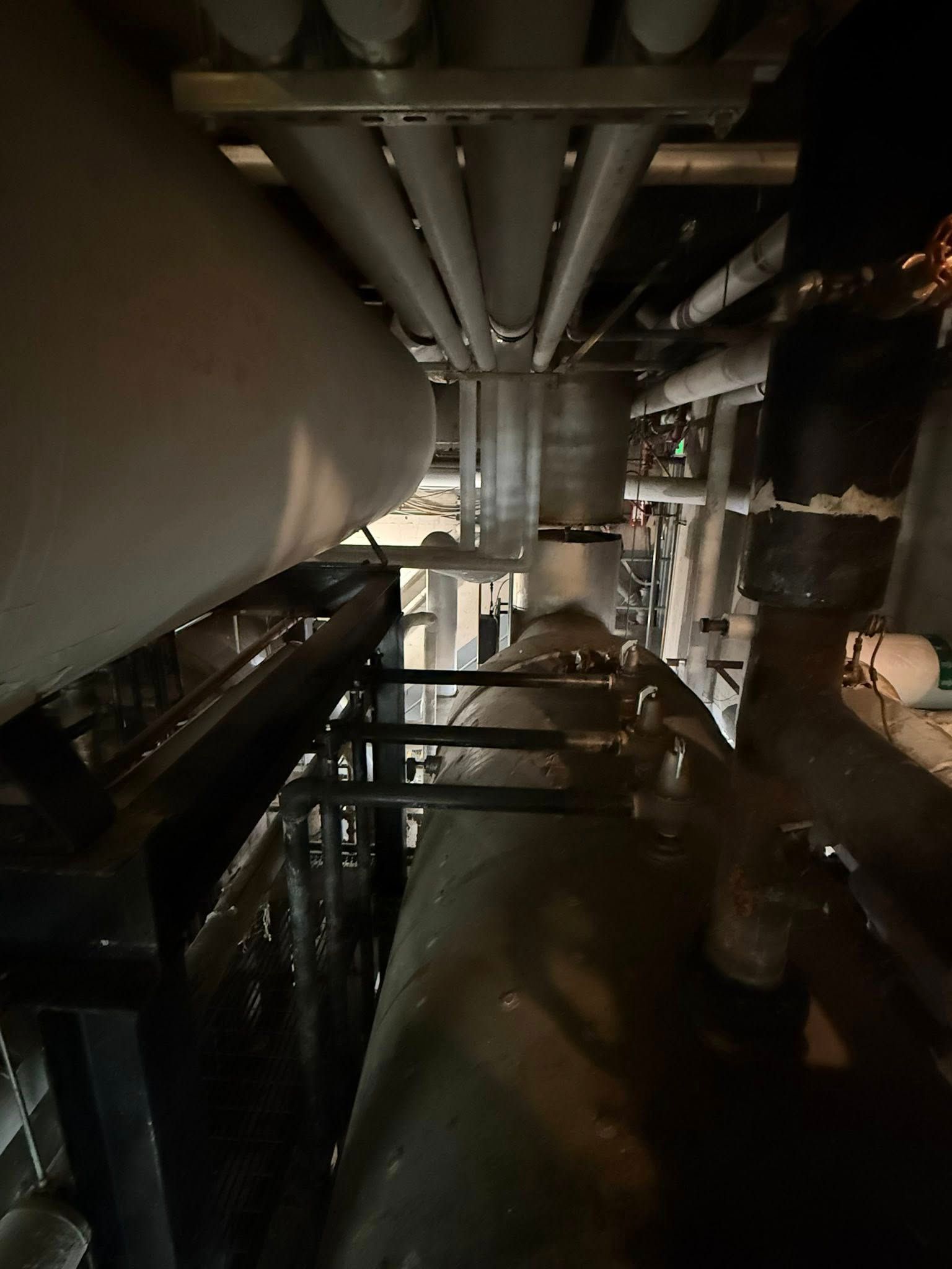 Industrial mechanical space featuring large metallic pipes and a dark, complex system of interconnected equipment.