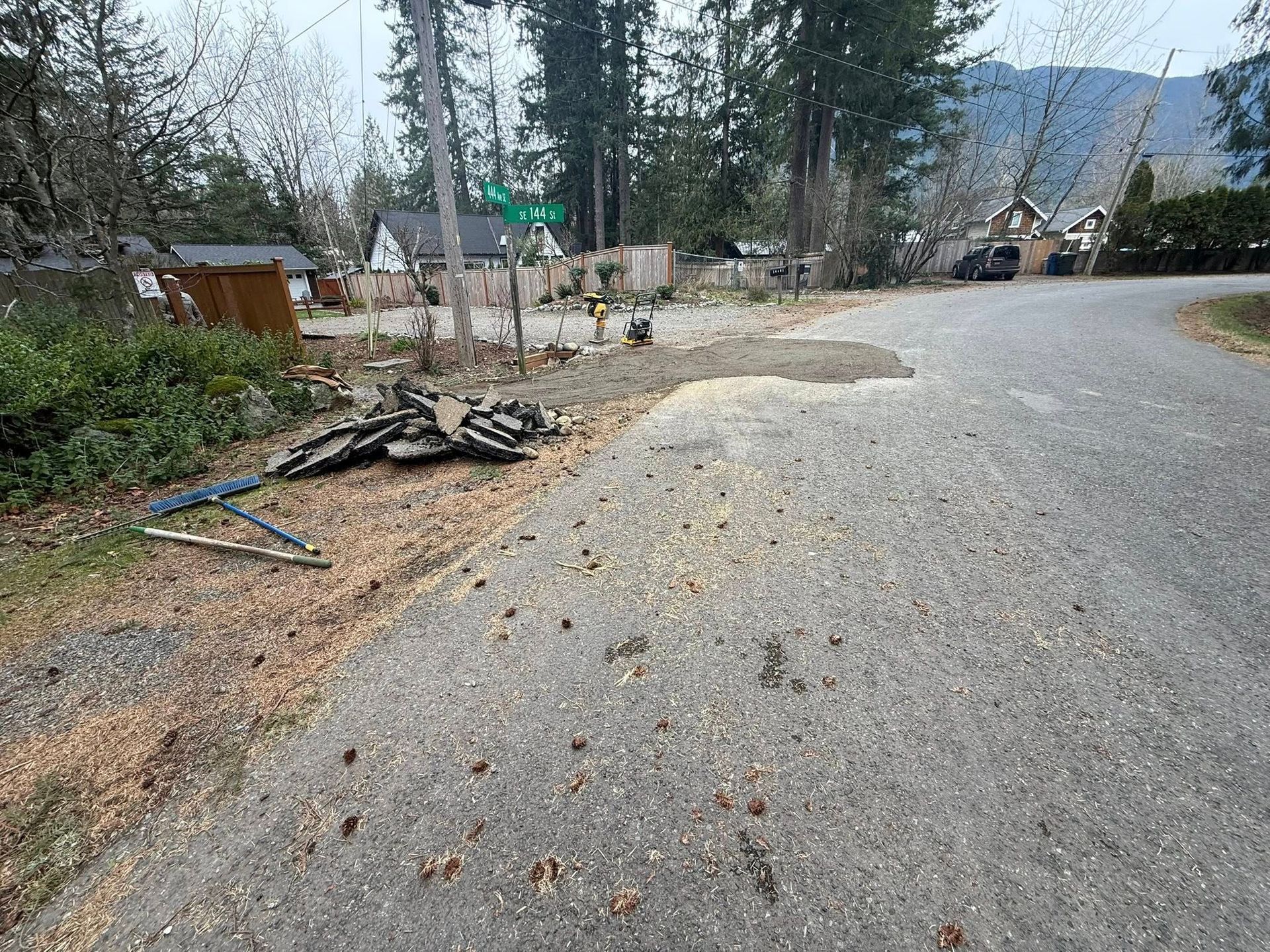 An unpaved road shoulder with a pile of discarded debris, a green street sign, and nearby trees under a cloudy sky.
