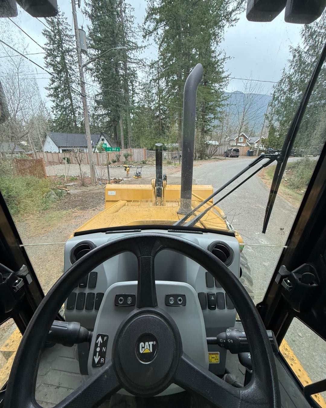 View from the cab of a yellow Caterpillar construction vehicle showing the steering wheel, hood, and exhaust pipe.