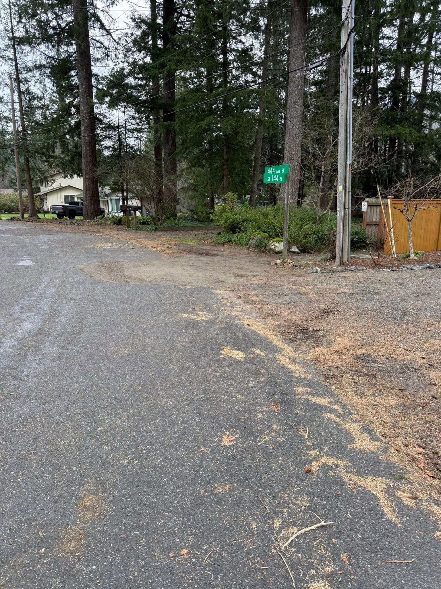 A gravel road leads into a wooded area with a small green street sign on a post and a wooden fence on the right.