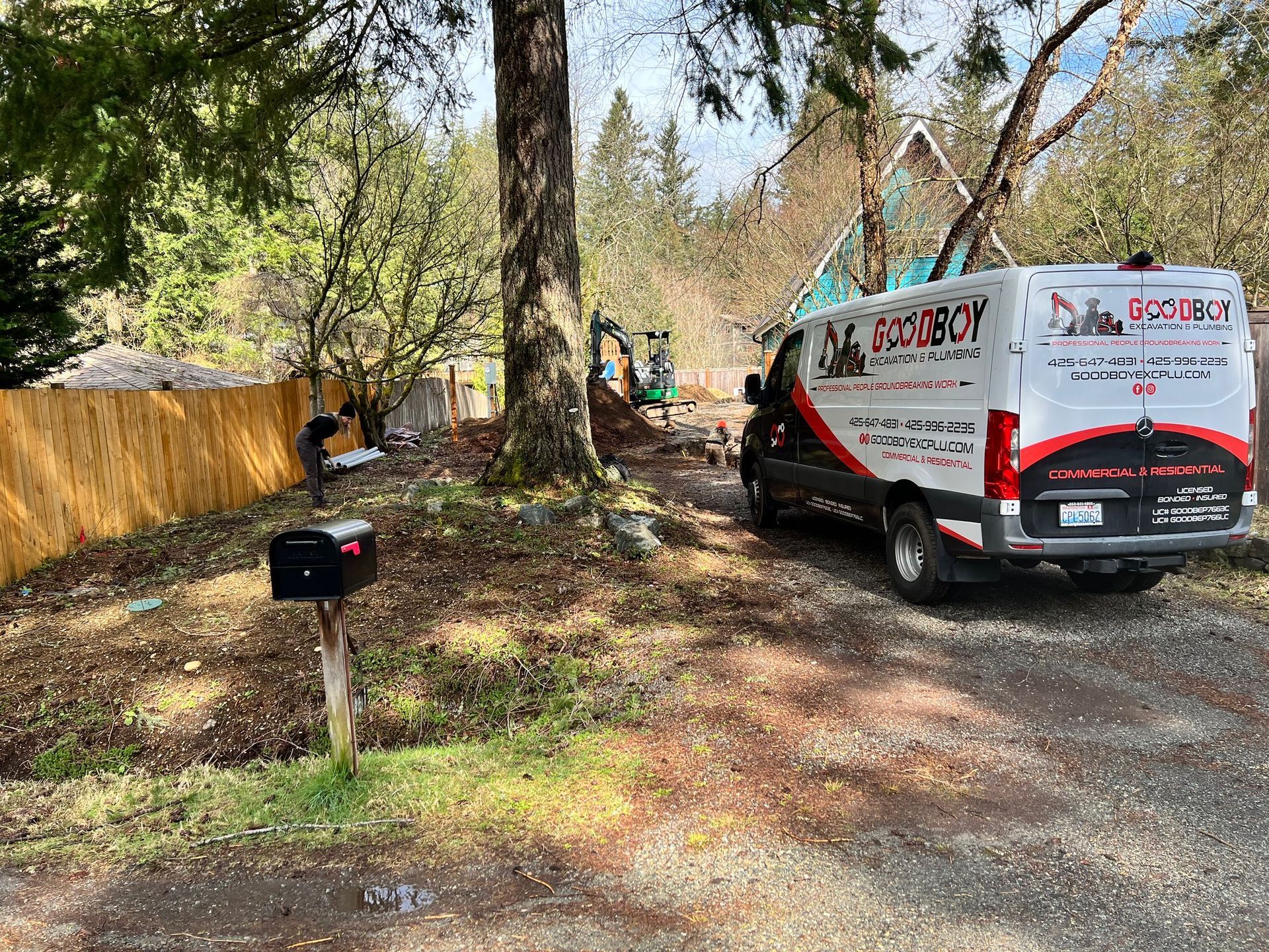 A white Dirtboy service van parked on a gravel driveway in front of a wooded lot with a wooden fence.