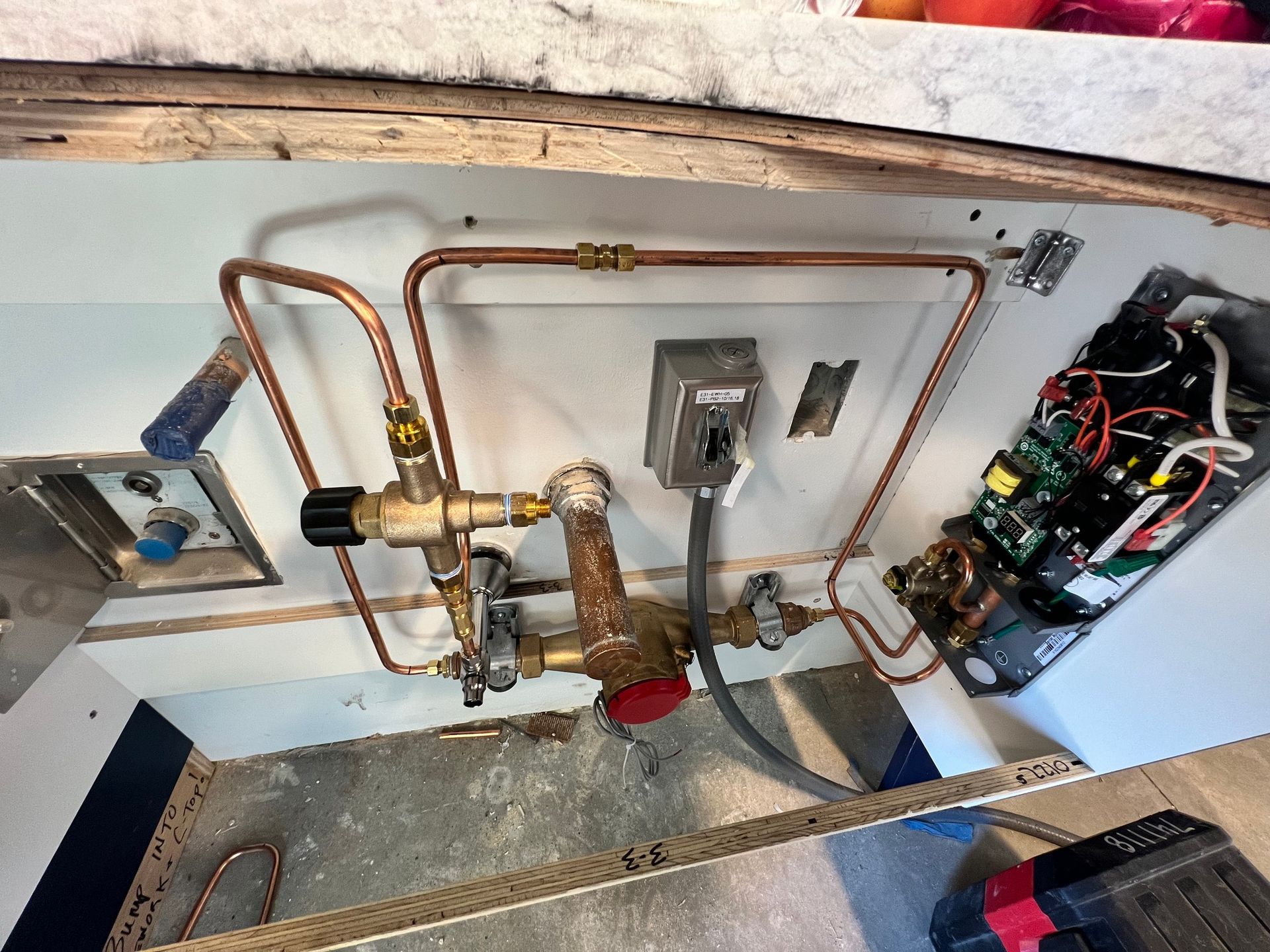 Under-sink view showing copper plumbing lines connected to a valve assembly, a power box, and electrical components.
