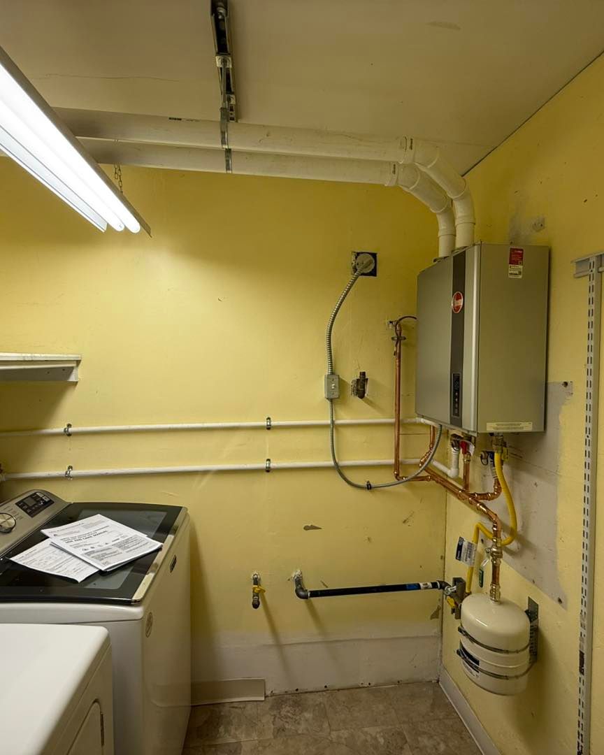 A laundry room wall features a wall-mounted tankless water heater, white supply lines, and a small expansion tank.
