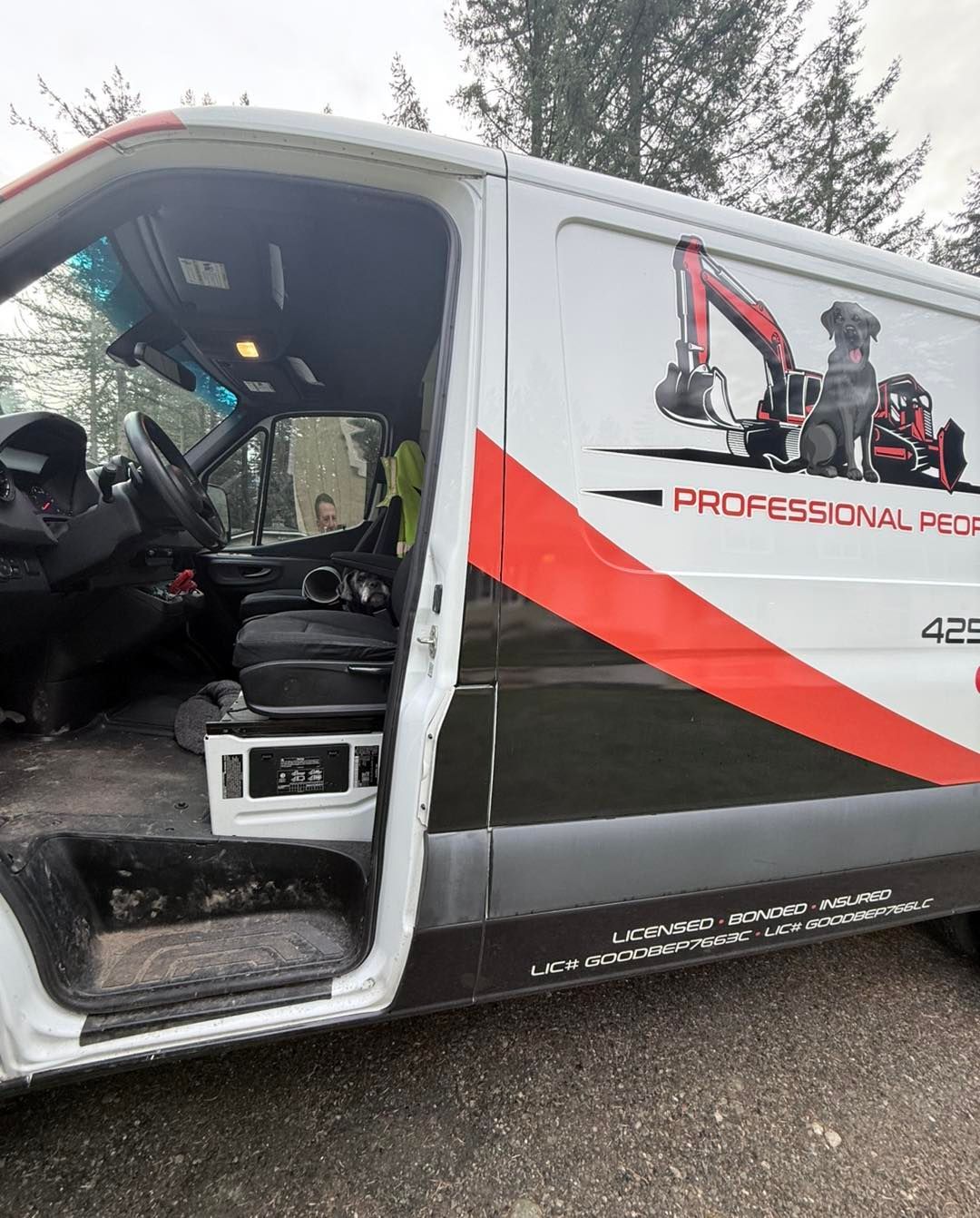 A white work van with open passenger door, black and red diagonal side graphics, and an excavator and dog logo.