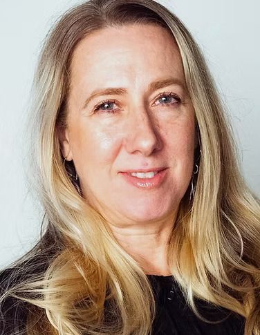 A portrait of a person with shoulder-length blonde hair and a neutral expression, positioned against a light background.