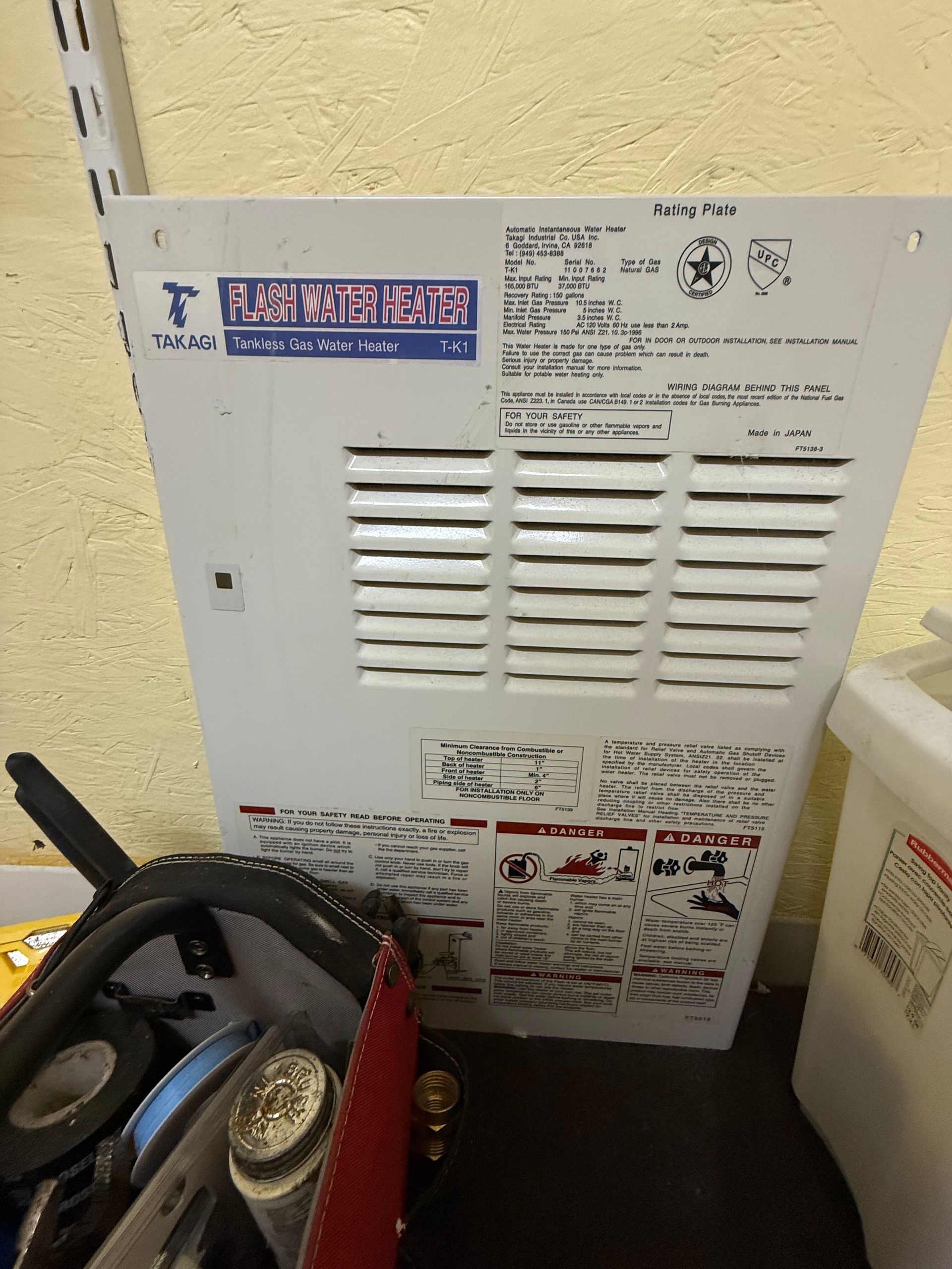 A metal Rainmaster irrigation controller panel with venting, model labels, and wiring instructions, leaning against a wall.