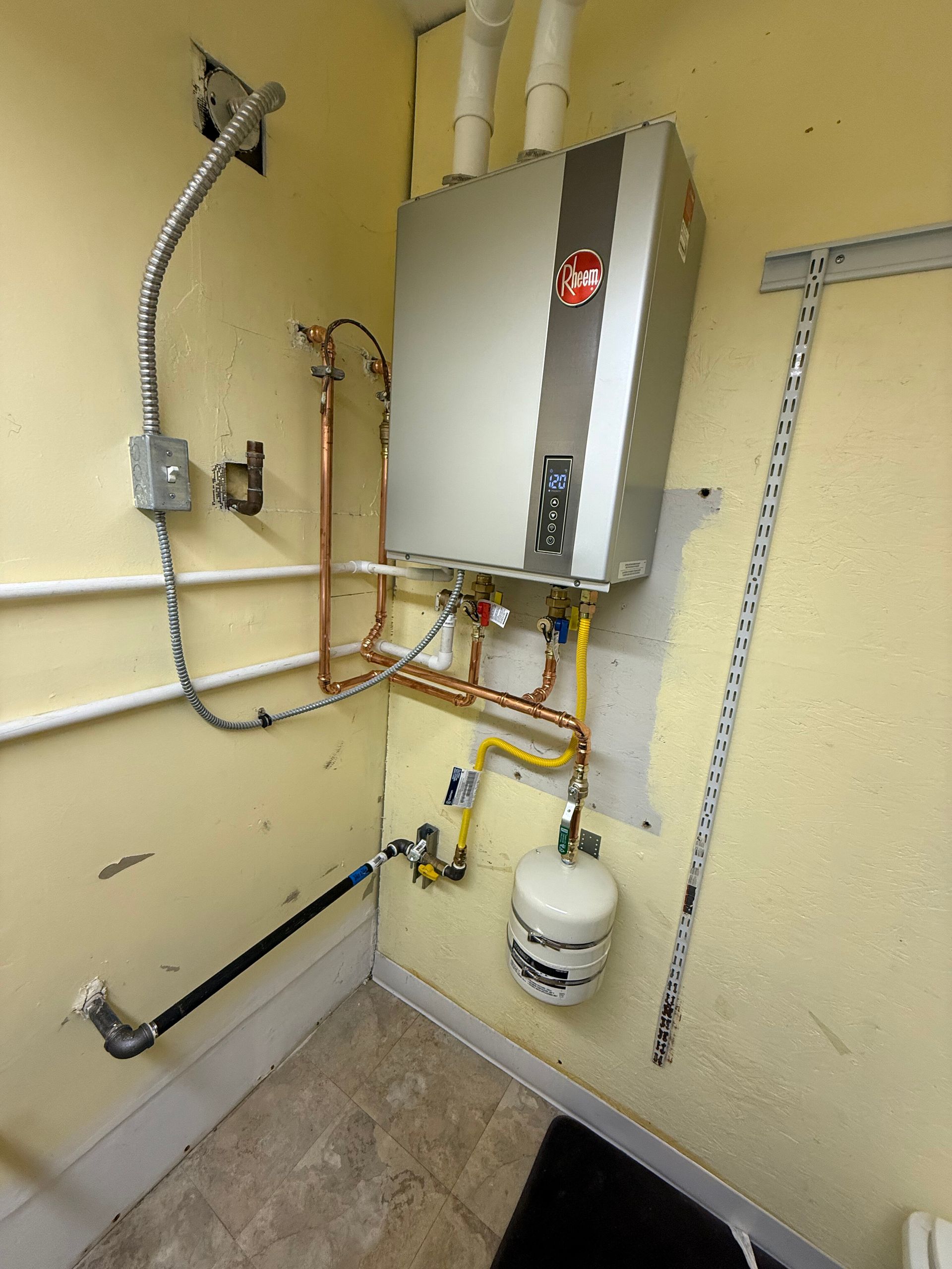 Tankless water heater with copper piping, a yellow gas line, and an expansion tank mounted on a pale yellow wall.
