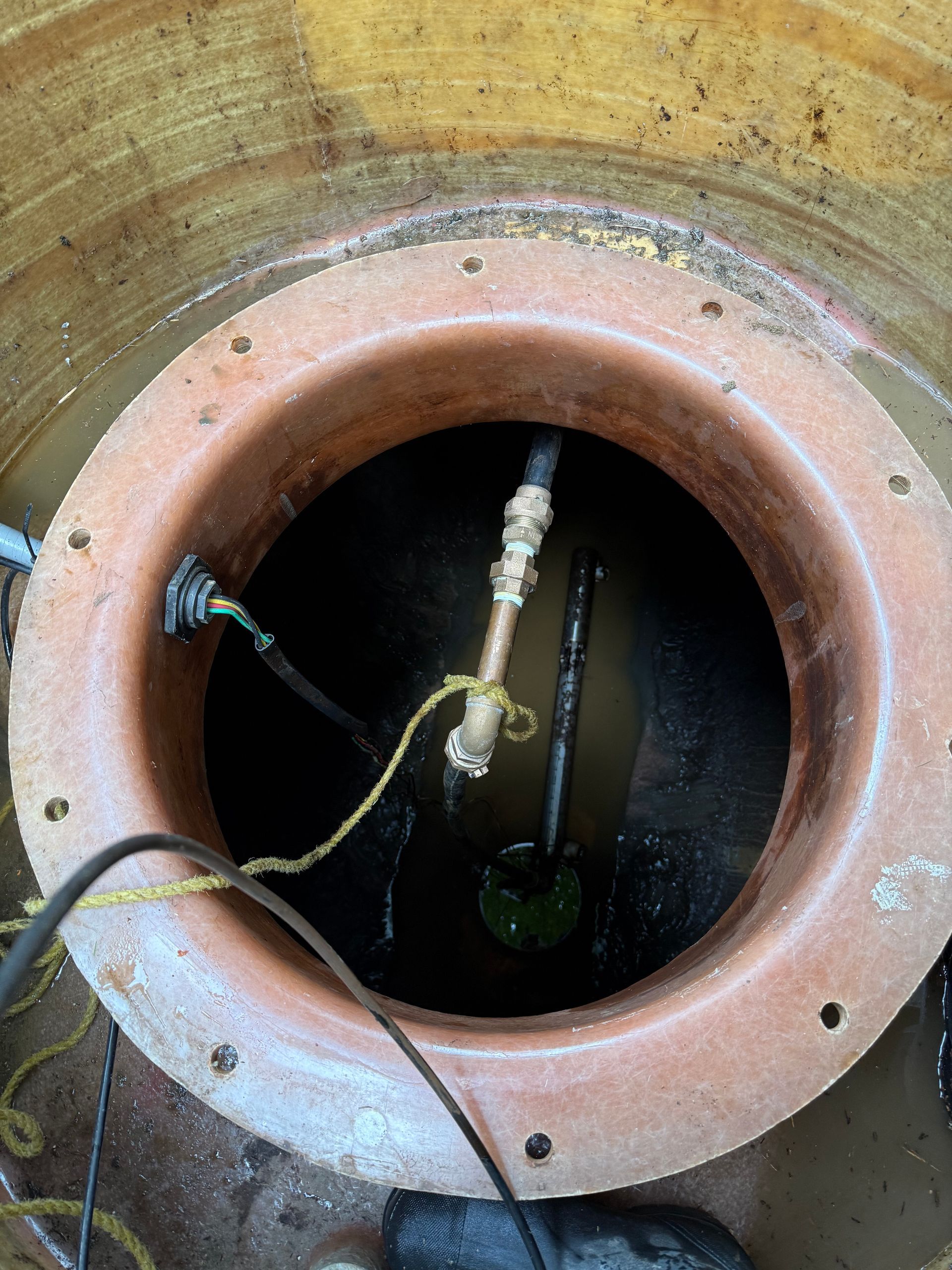 An open well or tank with a water pump, pipes, and electrical cables inside.