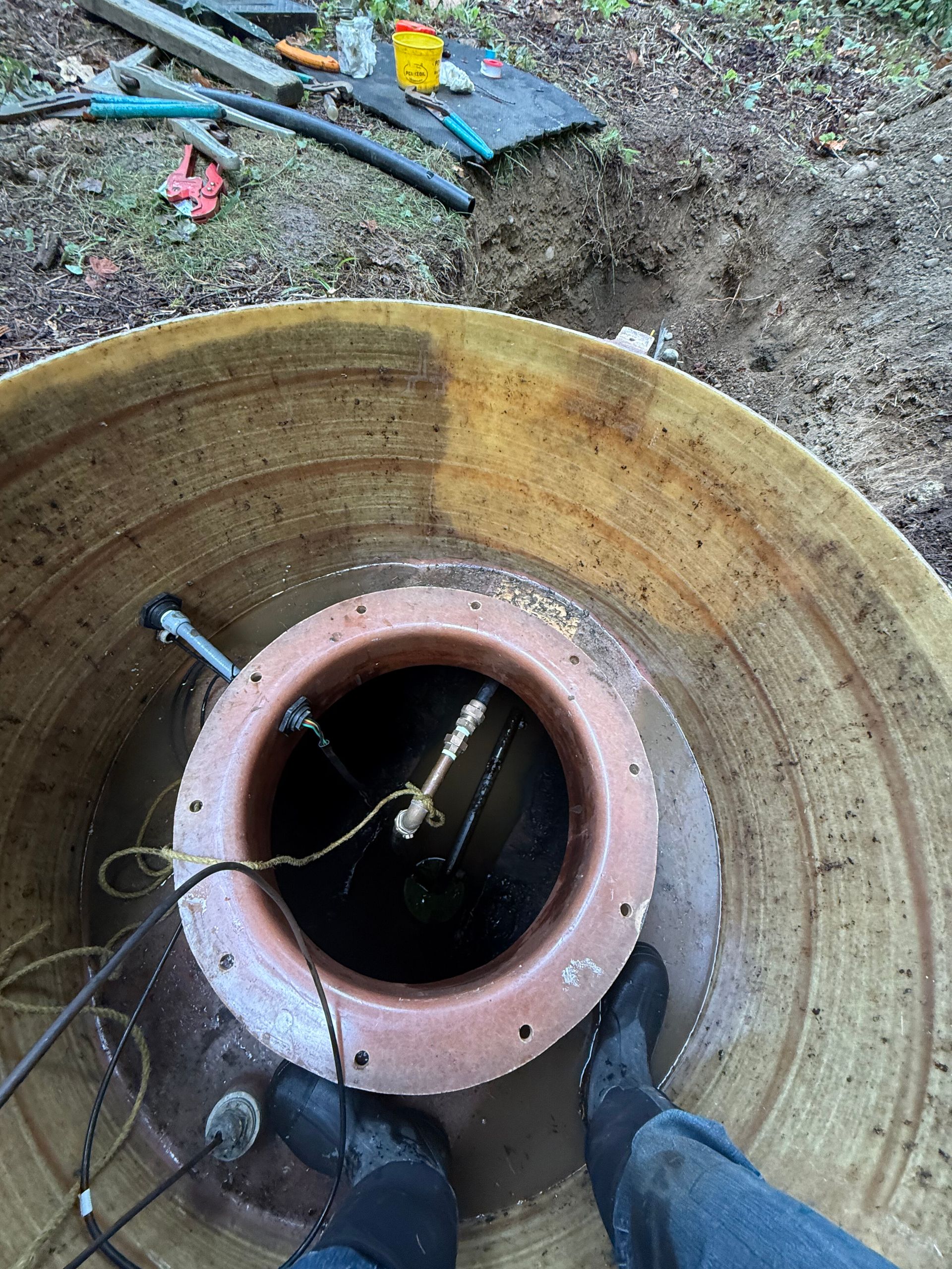 A person standing inside a large, circular, tiered fiberglass well casing, looking down into a narrower inner pipe.