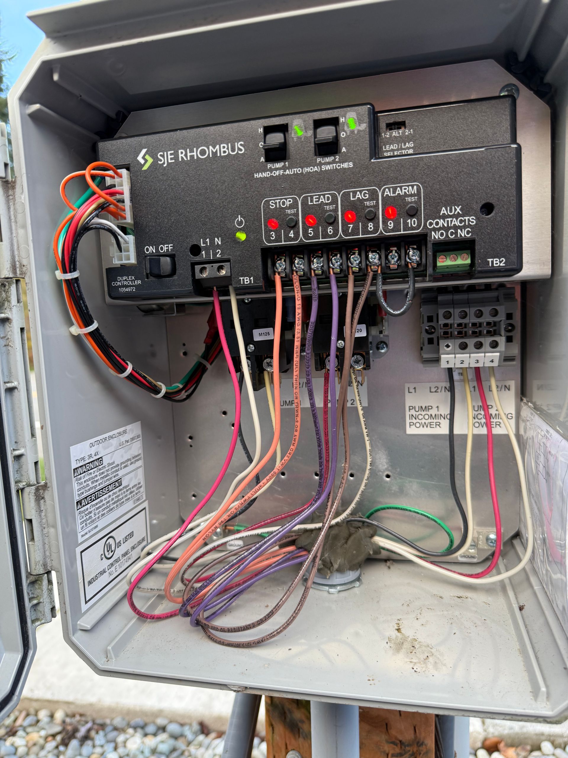 Open irrigation controller box mounted on a post, showing wired connections, circuit breakers, and status indicator lights.