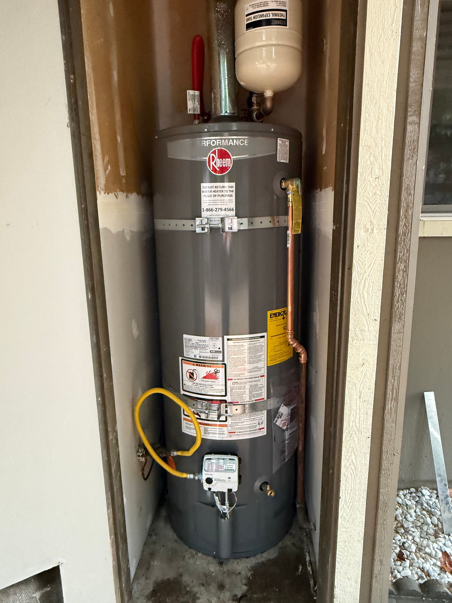 A gas water heater with a connected expansion tank installed in a recessed outdoor alcove.