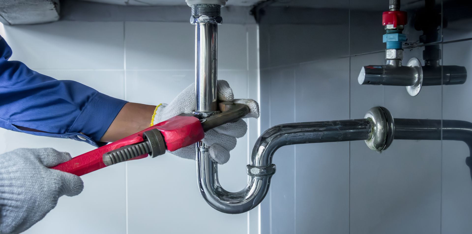 View of hands of a plumber fixing a sink with a wrench.