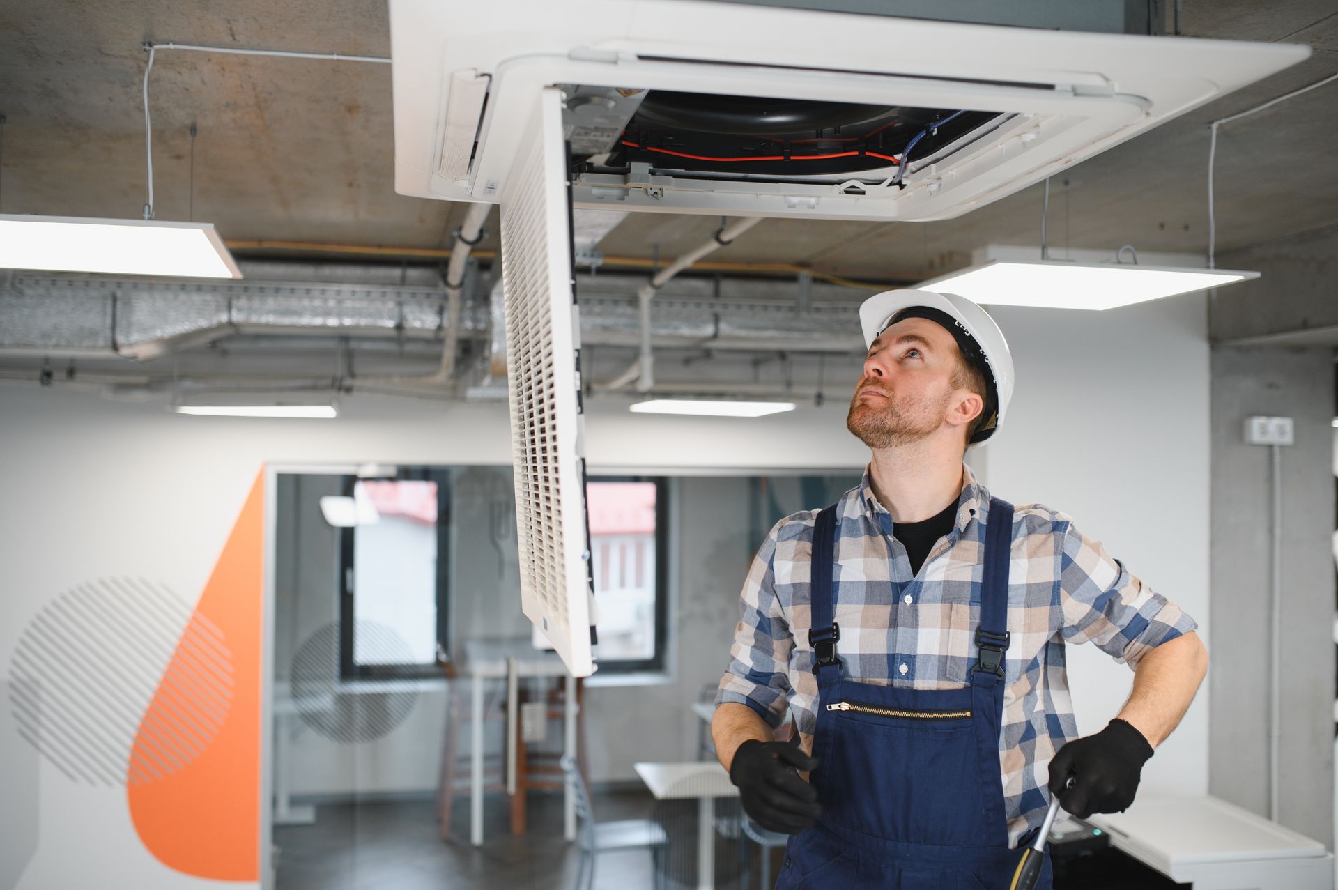 Commercial heating contractor inspecting ceiling HVAC unit in modern office building. Commercial heating contractor inspecting ceiling HVAC unit in modern office building.