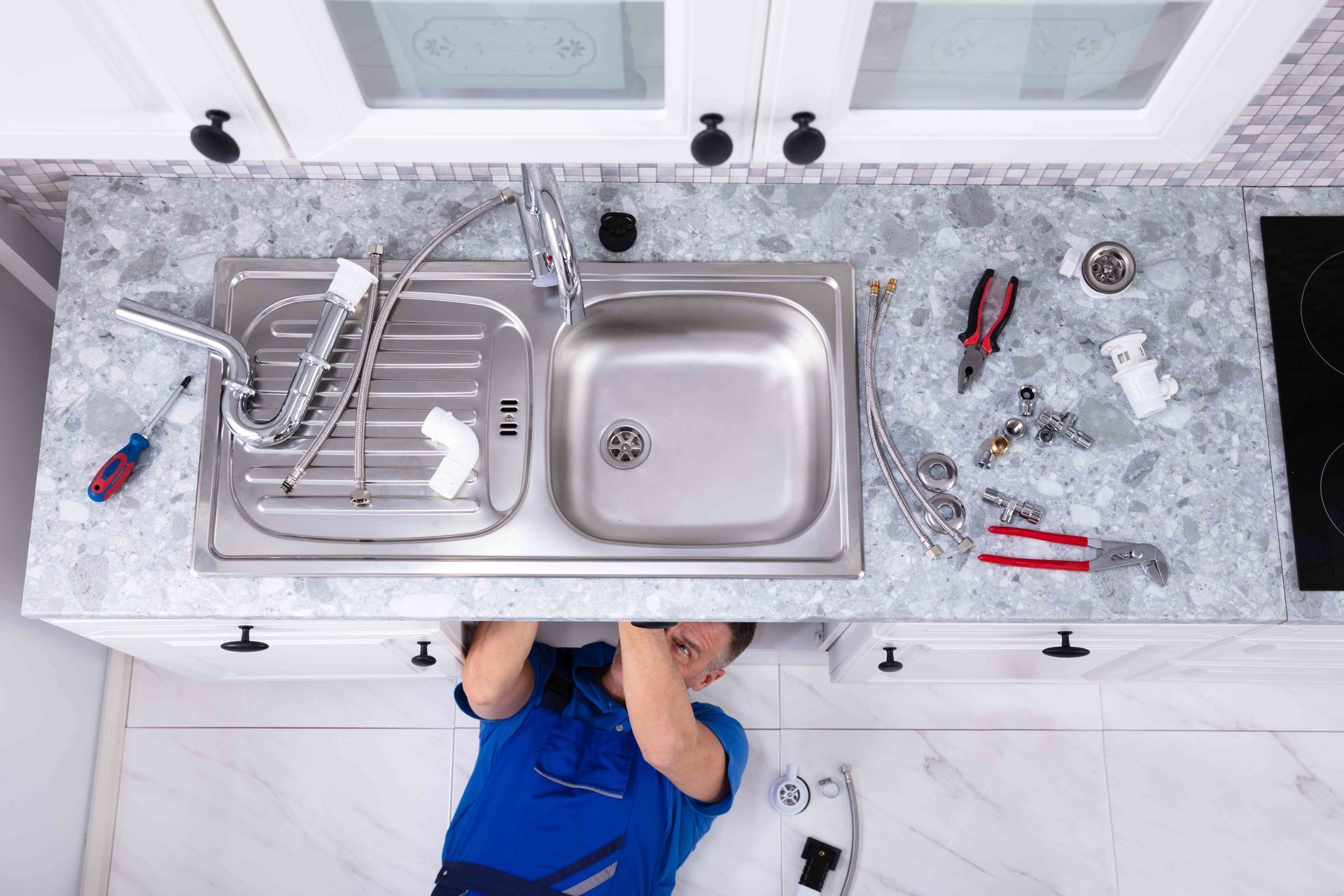 Plumber repairing kitchen sink pipes with tools and fittings.