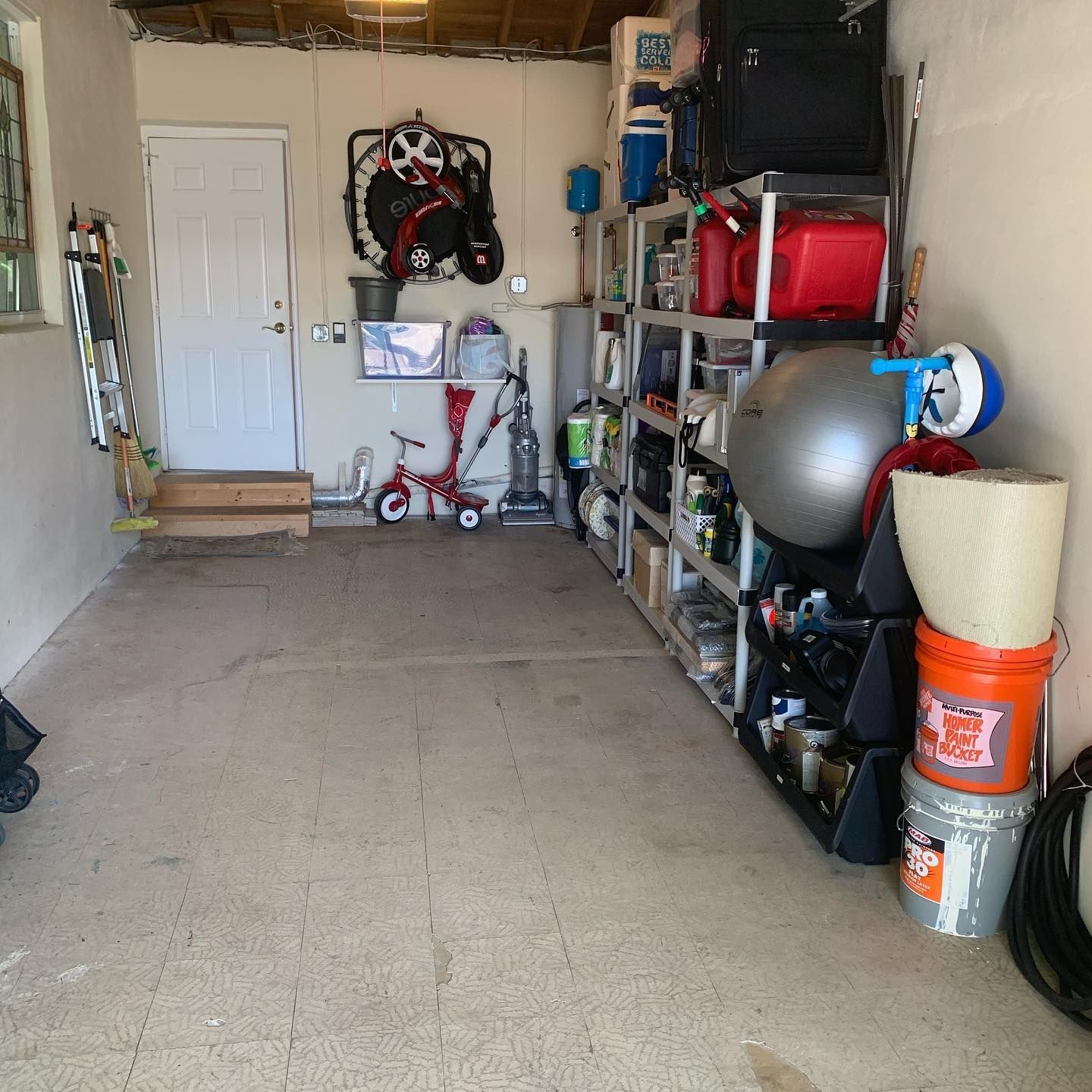 A cluttered garage interior with a door, shelves holding various items, and some sporting equipment hanging on the wall.