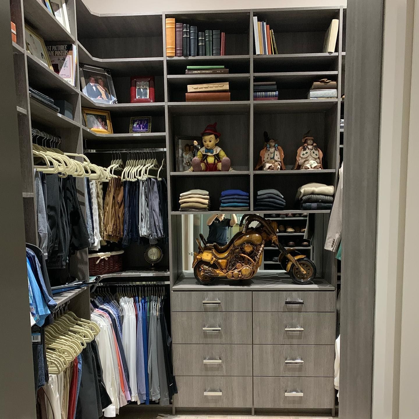 Walk-in closet with gray shelving, drawers, and clothing. Display items include books, figurines, and clothes.