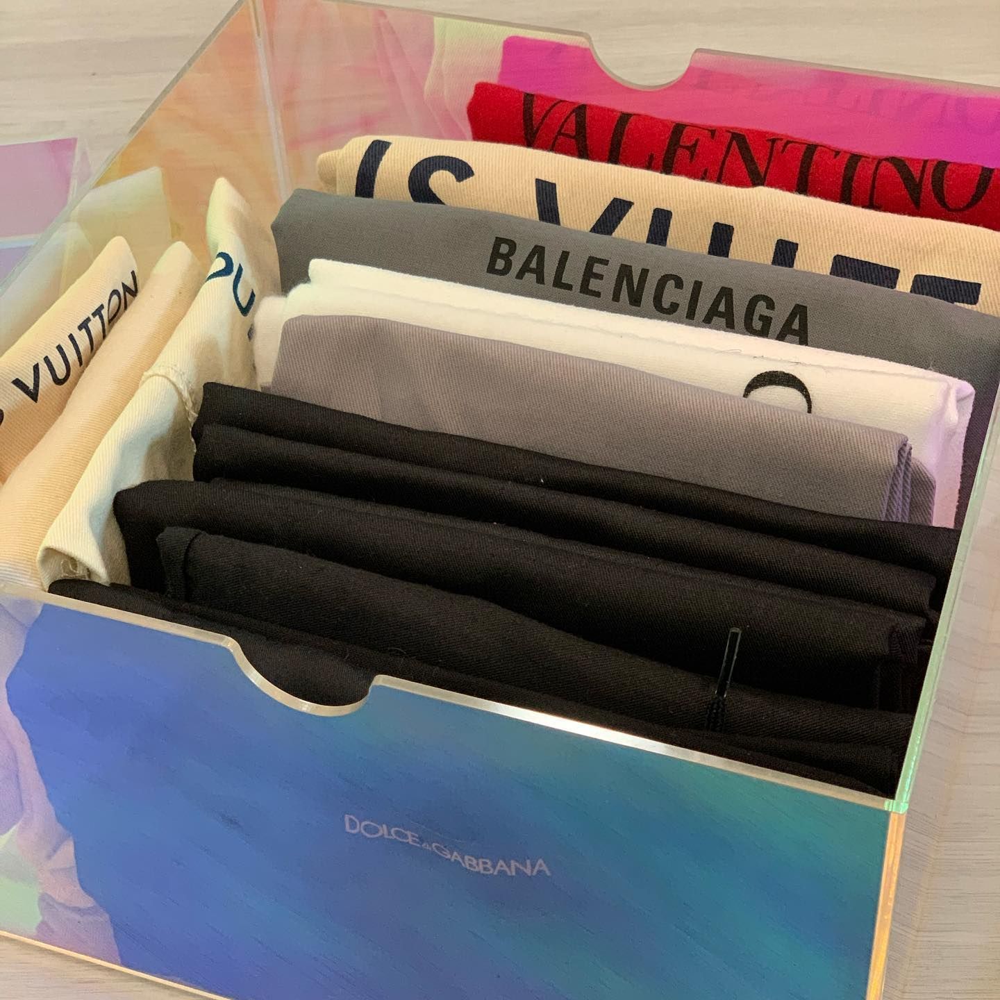 A box with folded luxury brand clothing, including Valentino, Balenciaga, and Dolce & Gabbana.