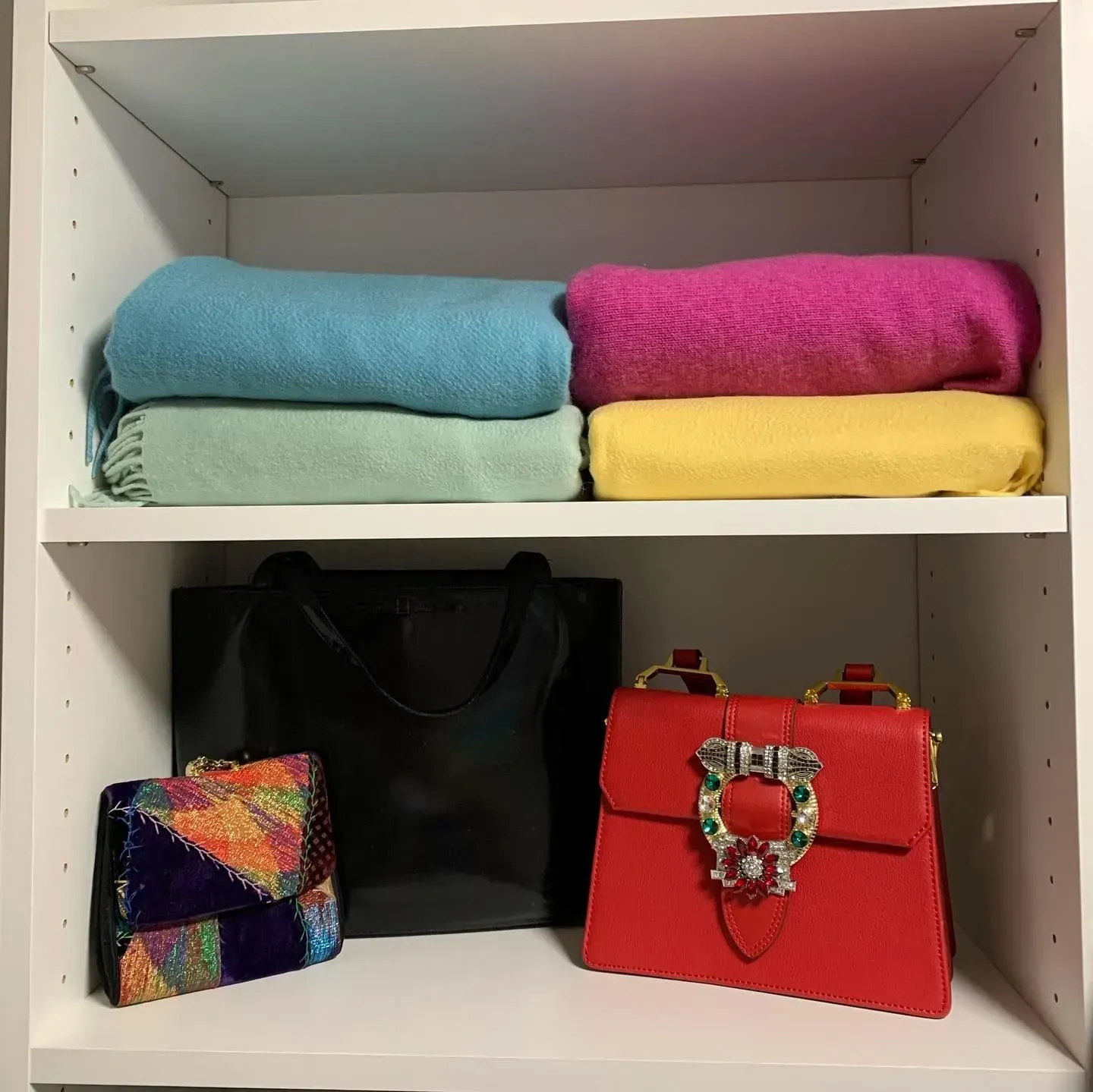 A red purse sits on a shelf next to a black bag