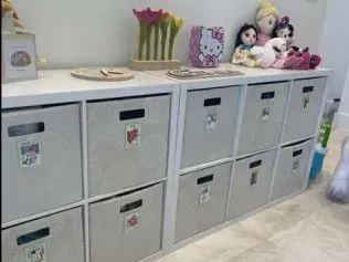 A room with a shelf filled with lots of bins and dolls.