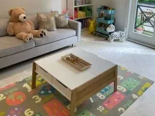 A living room with a couch , table , rug and teddy bear.