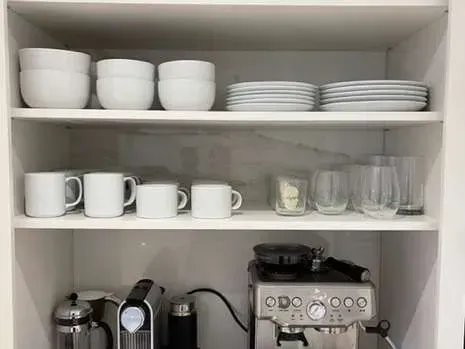 A kitchen cabinet filled with plates , cups , and a coffee maker.