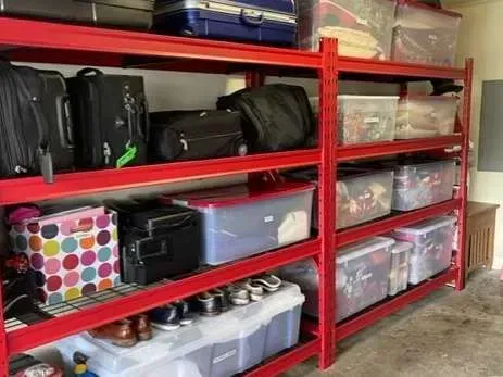 A bunch of luggage is sitting on a red rack in a garage.