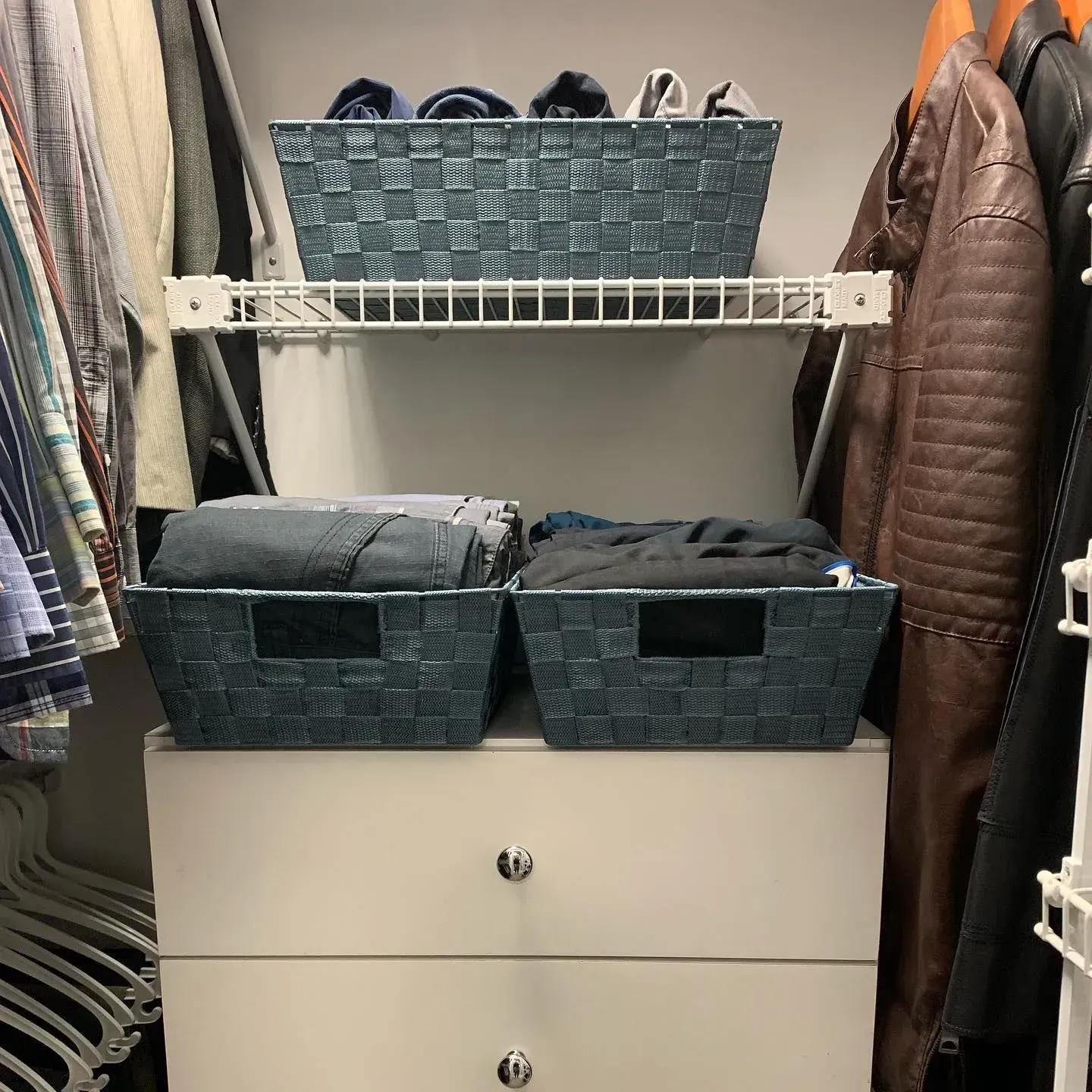 Two baskets are sitting on top of a white dresser in a closet.