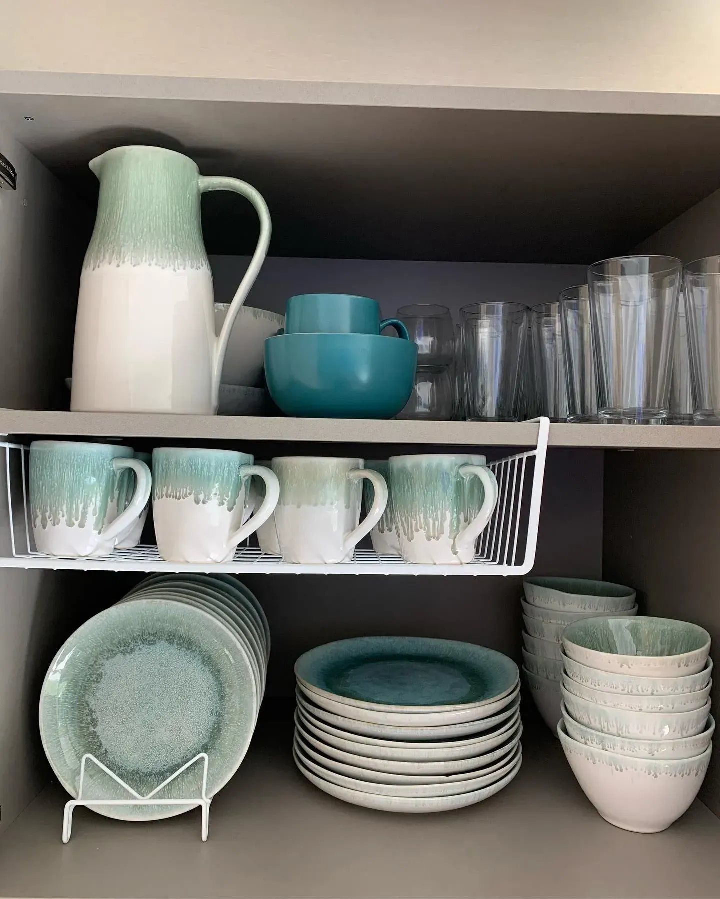 A kitchen cabinet filled with plates , cups , bowls and glasses.