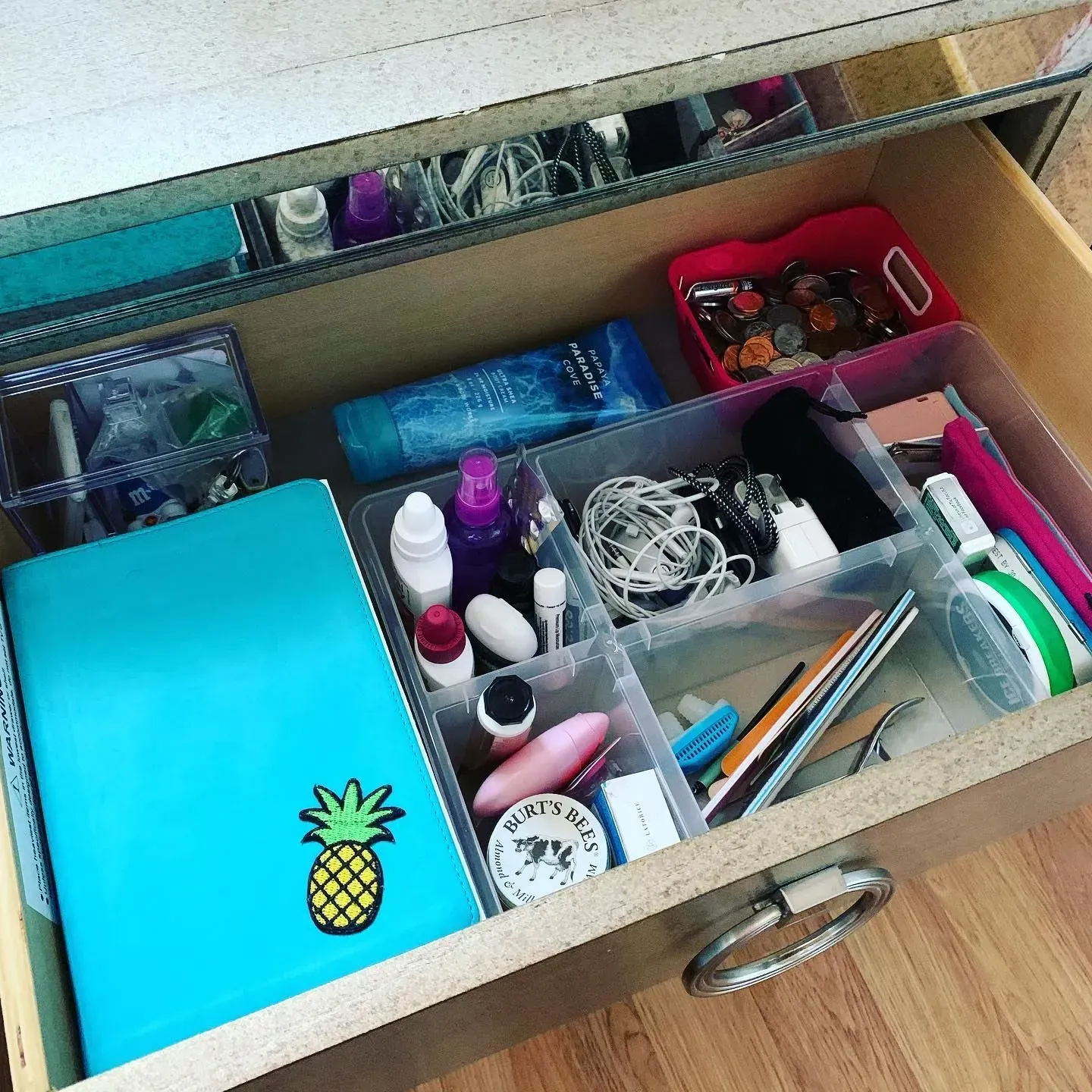 A drawer filled with various items including a notebook with a pineapple on it