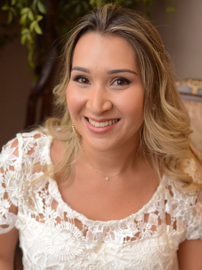A woman in a white lace top is smiling for the camera.