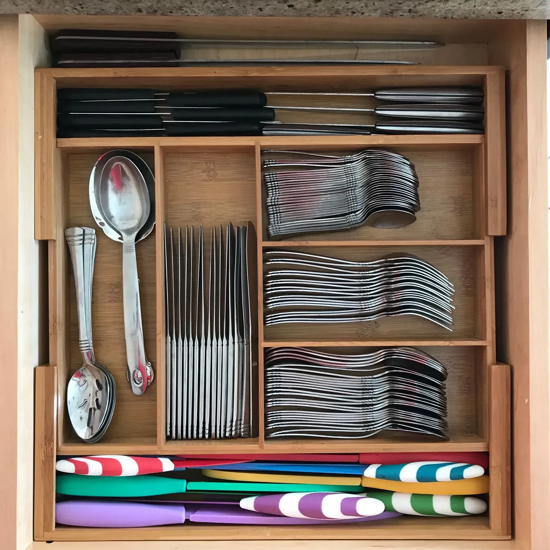 A wooden drawer filled with silverware including spoons knives and forks