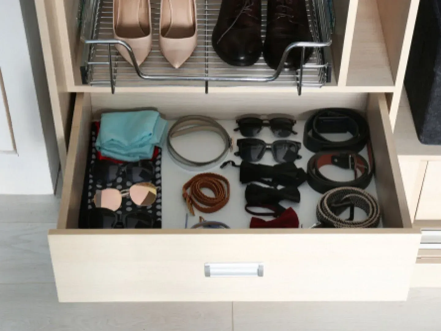 A drawer in a closet filled with shoes , belts , sunglasses and other items.