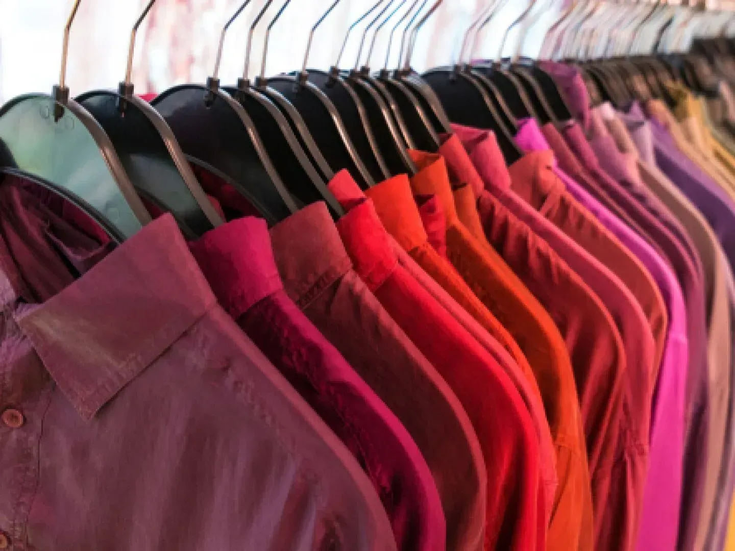 A row of colorful shirts are hanging on a rack