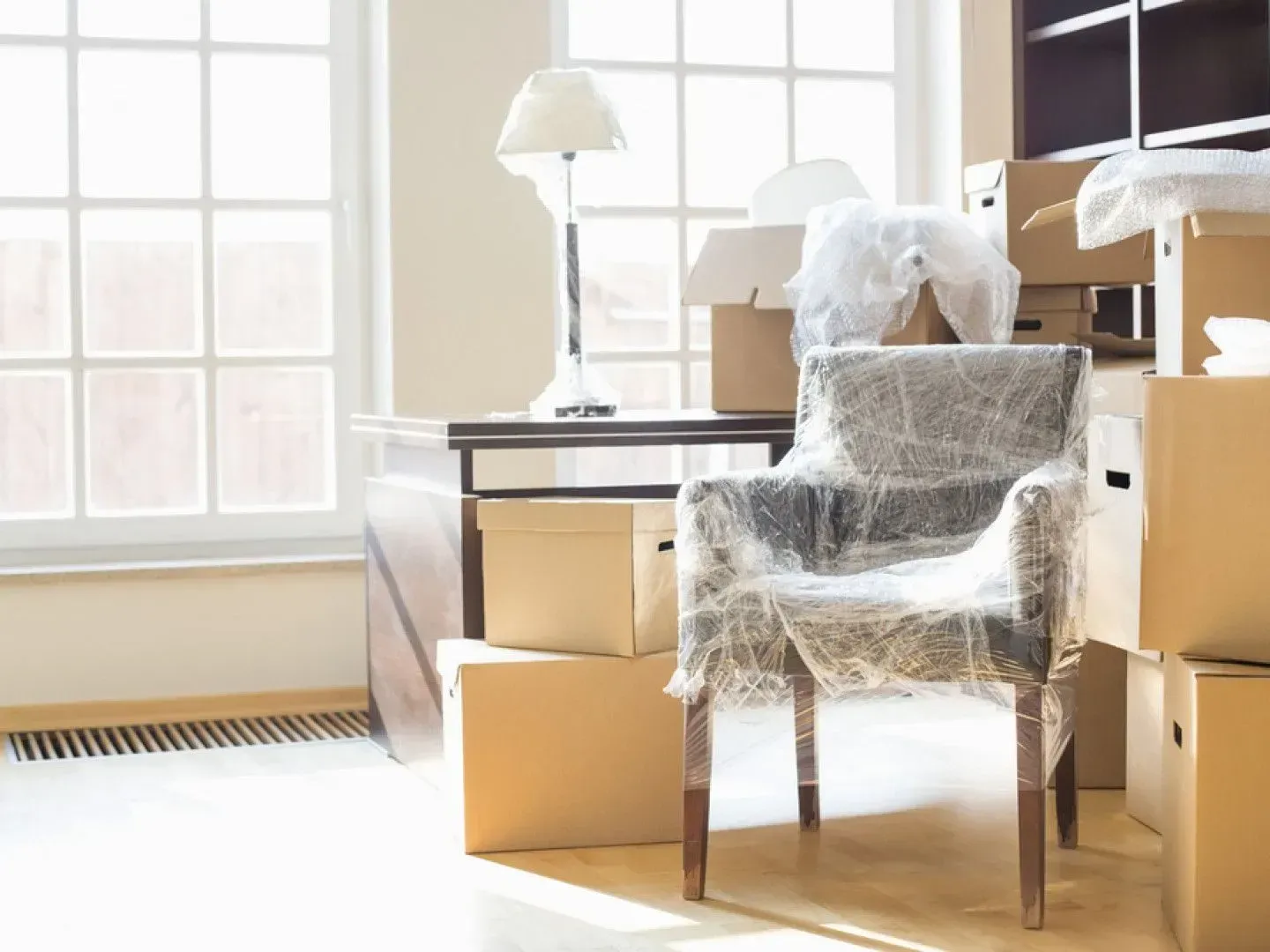 A chair is wrapped in plastic in a room filled with cardboard boxes.