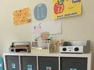 A room with a shelf , a stove , and a drawing on the wall.