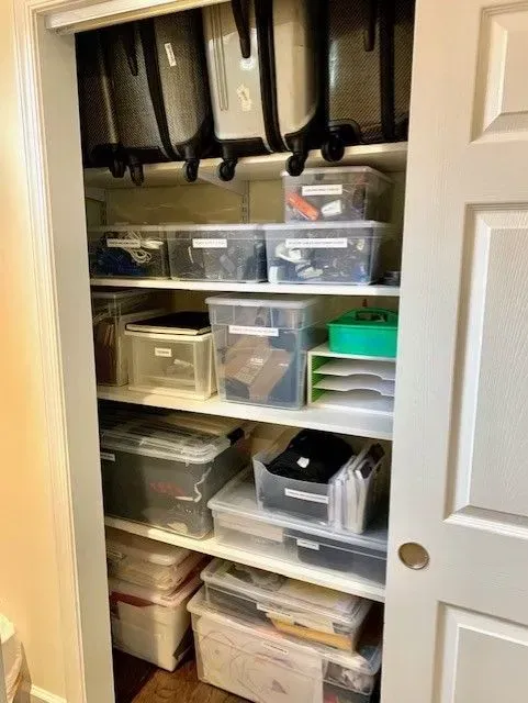 A closet filled with lots of plastic bins and suitcases.