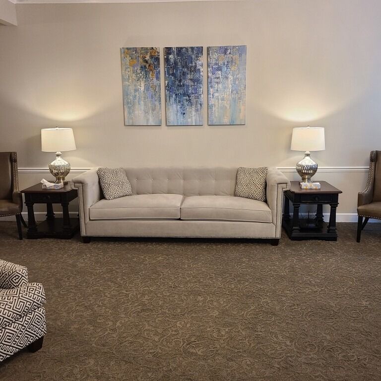 A neutral-toned sofa sits between two dark side tables with lamps, below a three-piece blue and gold abstract art set.