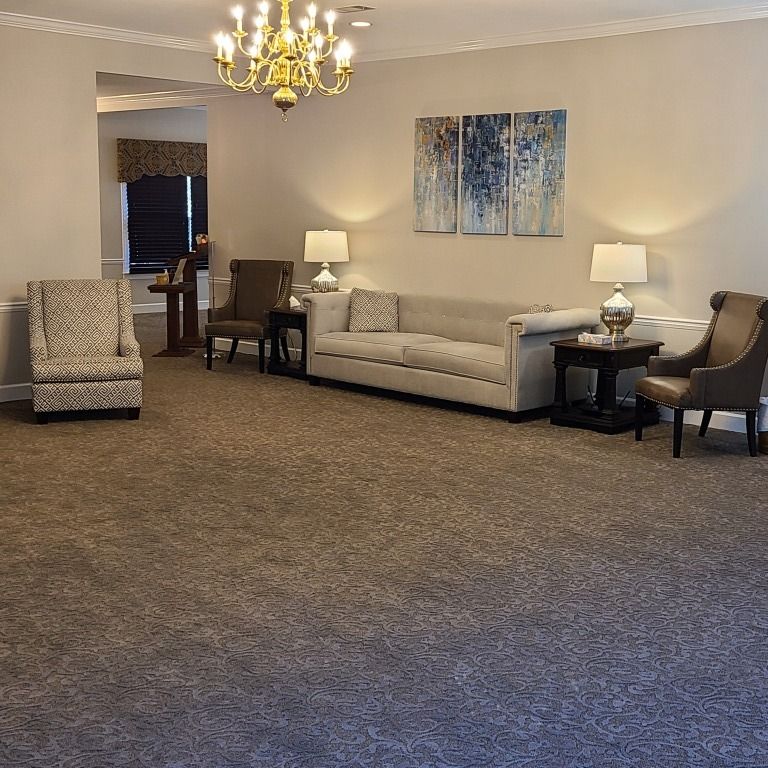 A neutrally toned waiting room with a sofa, armchairs, two lamps, a chandelier, and wall art.