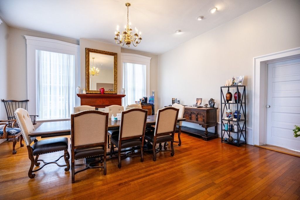 A formal dining room features a long table with five upholstered chairs, a fireplace with a mirror, and wood flooring.