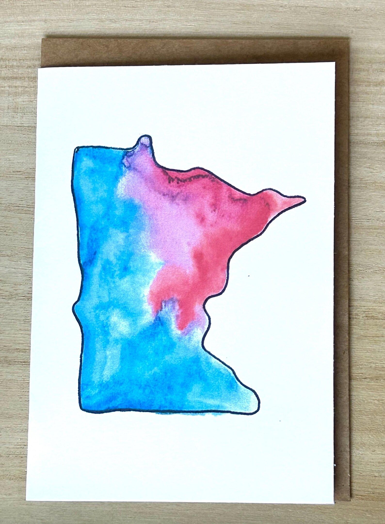 Watercolor painting of Minnesota in blue and pink, on a white card with a brown envelope.