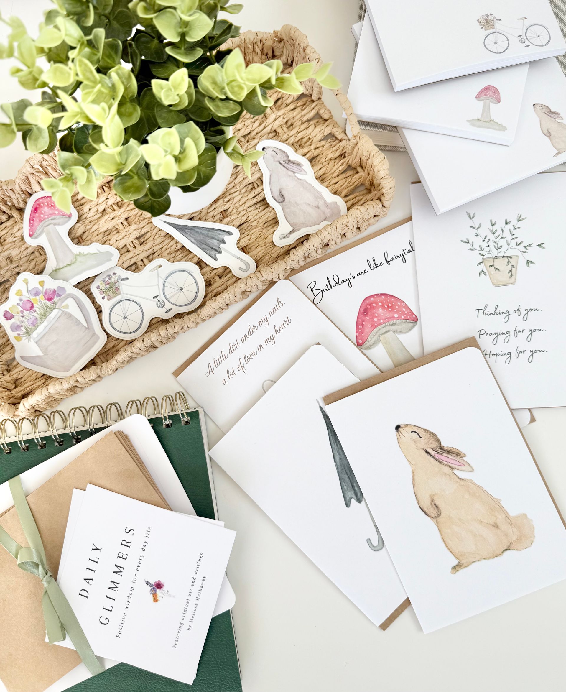 Cards, envelopes, and stickers featuring illustrations of a bunny, bicycle, and mushrooms, near greenery.