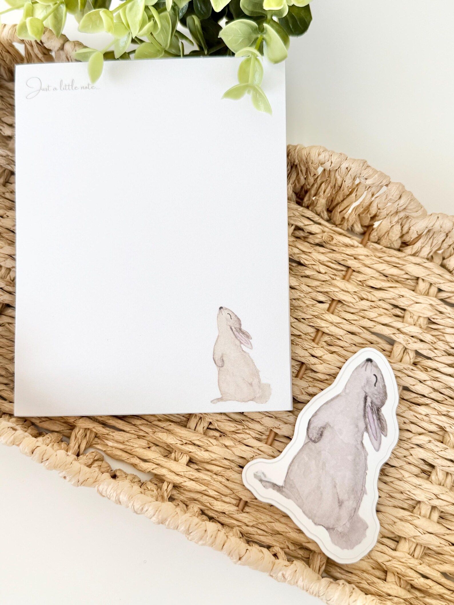 White notepad with bunny illustration and separate bunny sticker on woven mat.
