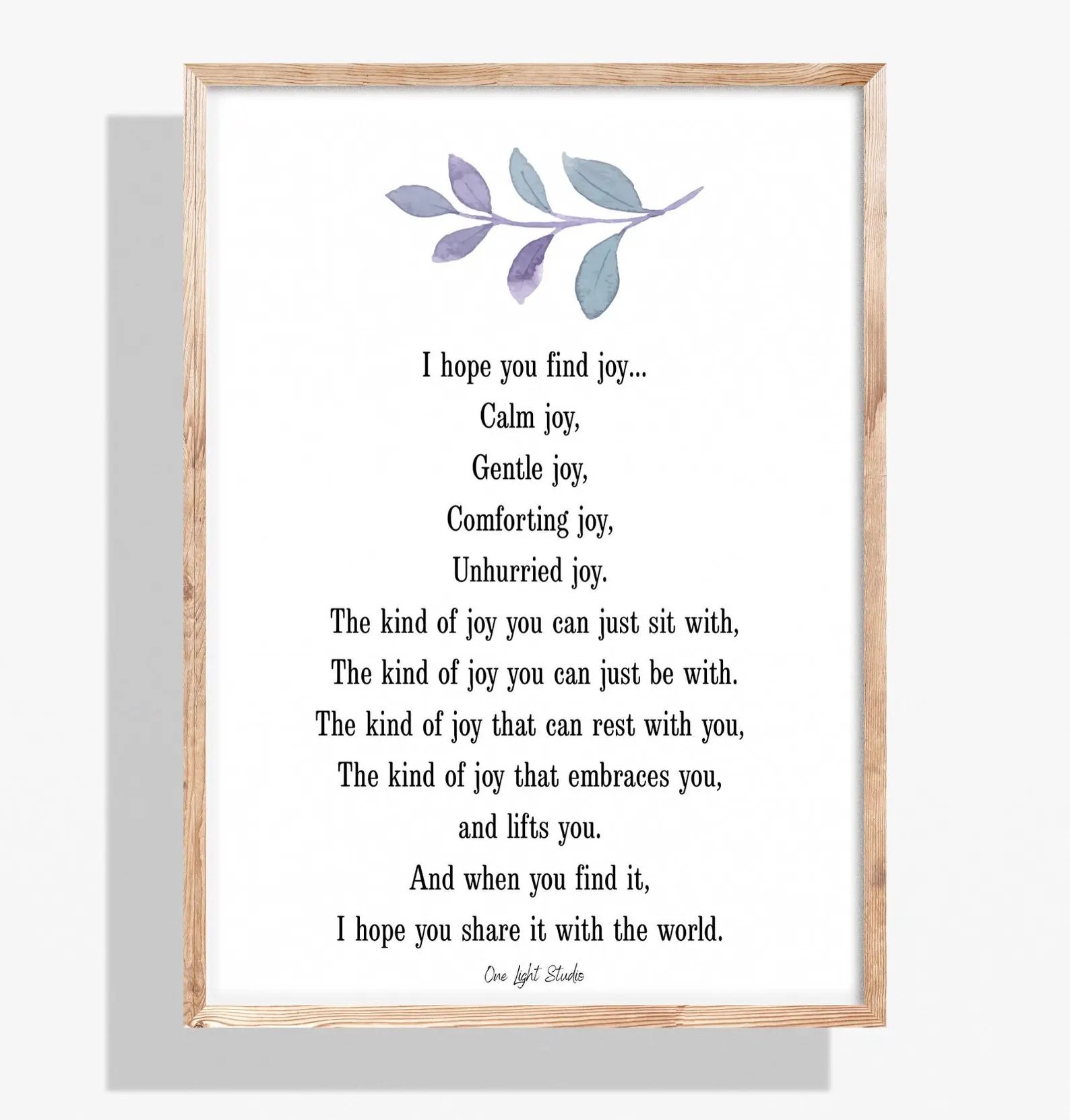 A framed print with a light wood frame. It features a watercolor leaf design and a poem about finding joy.