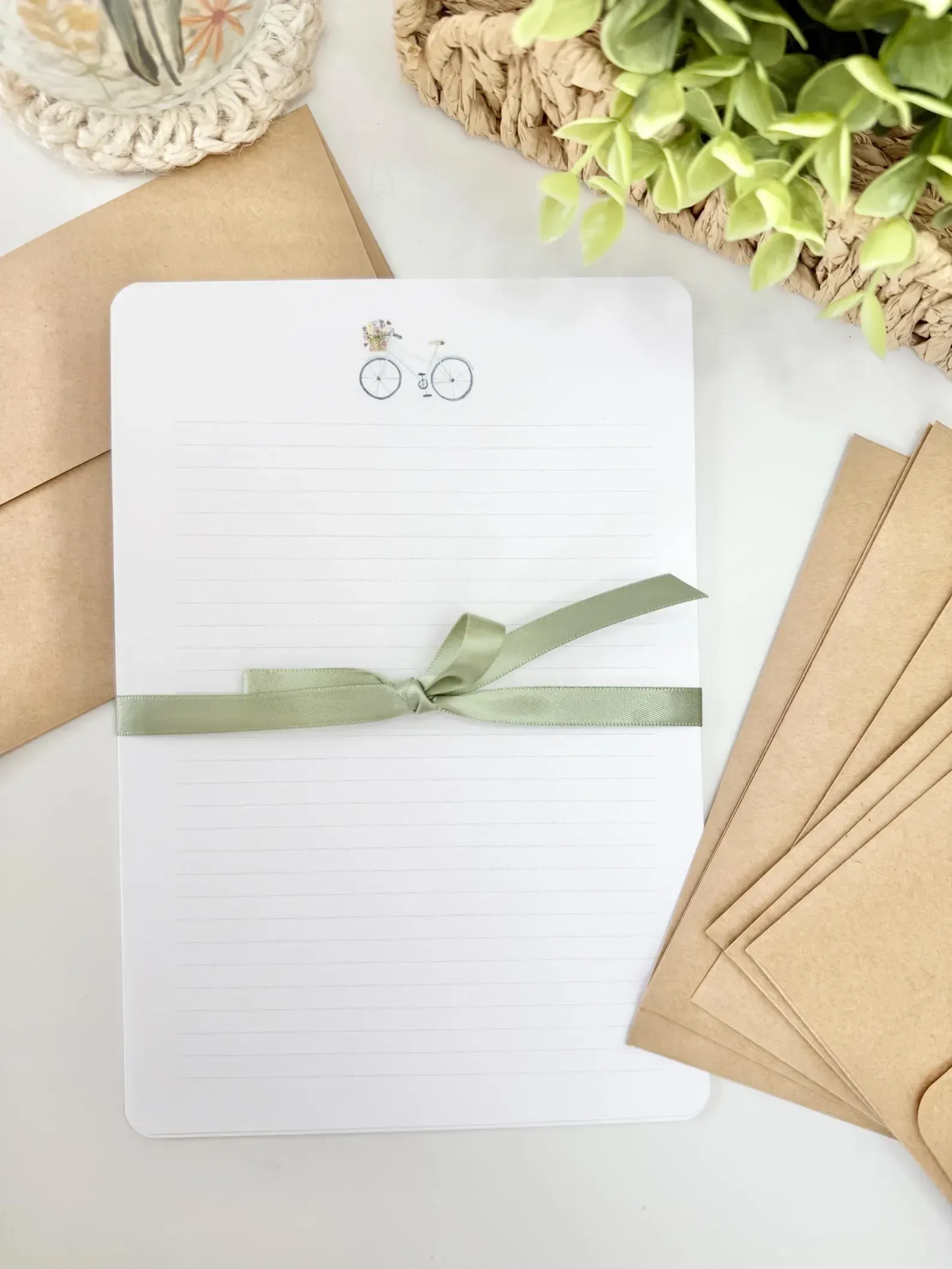 Stationery set: lined paper with bicycle drawing, green ribbon, kraft envelopes.