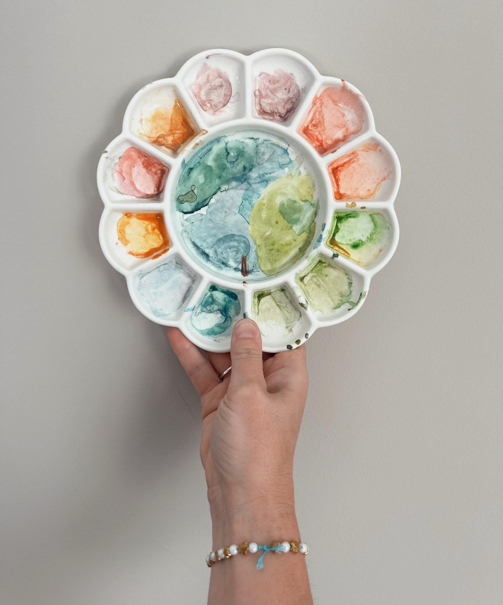Hand holding a white paint palette with colorful watercolor paints.