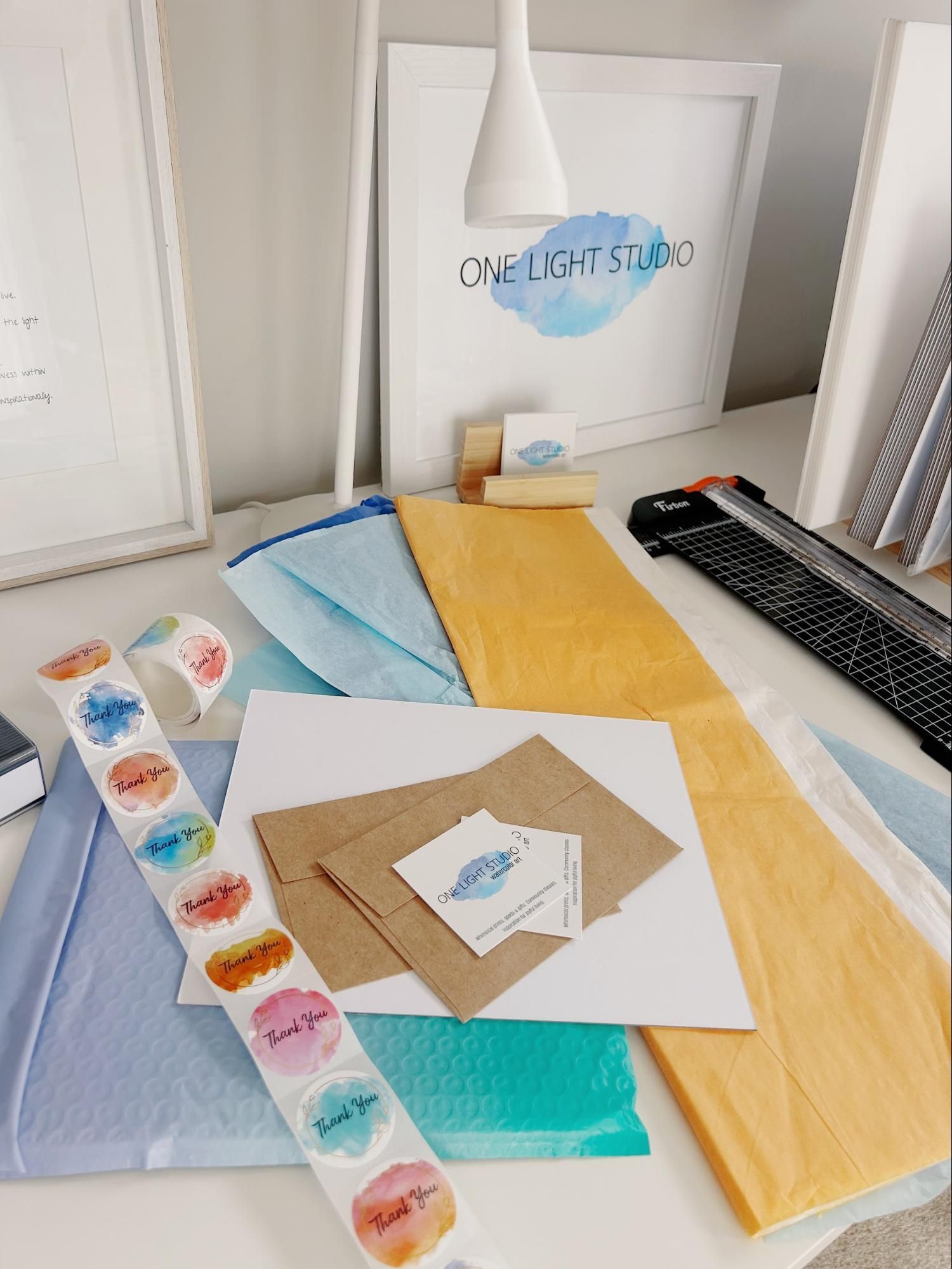 Stationery setup with packaging supplies and thank you stickers on a white table;