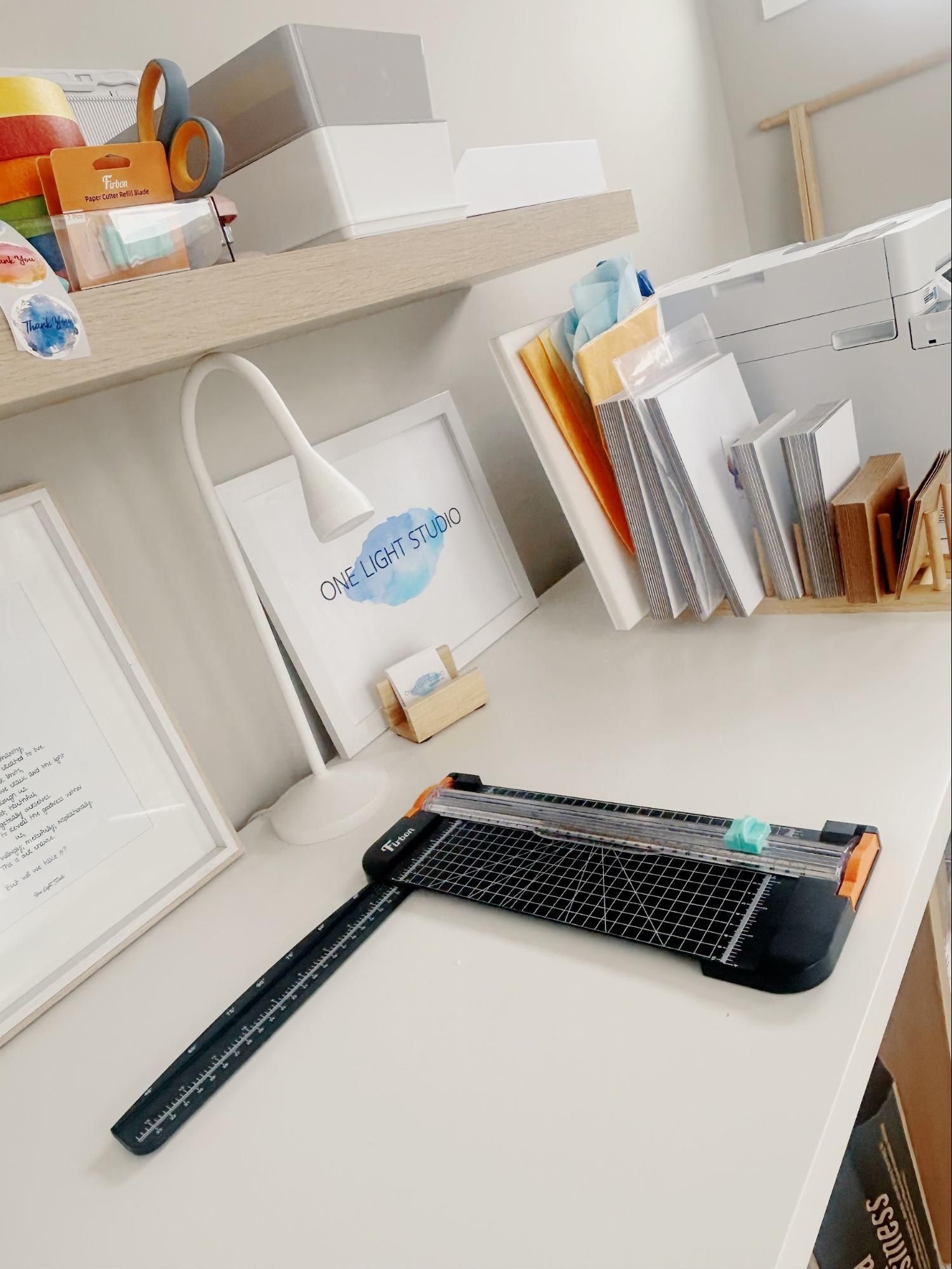 Paper cutter on a white desk, with supplies on a shelf and books to the right.